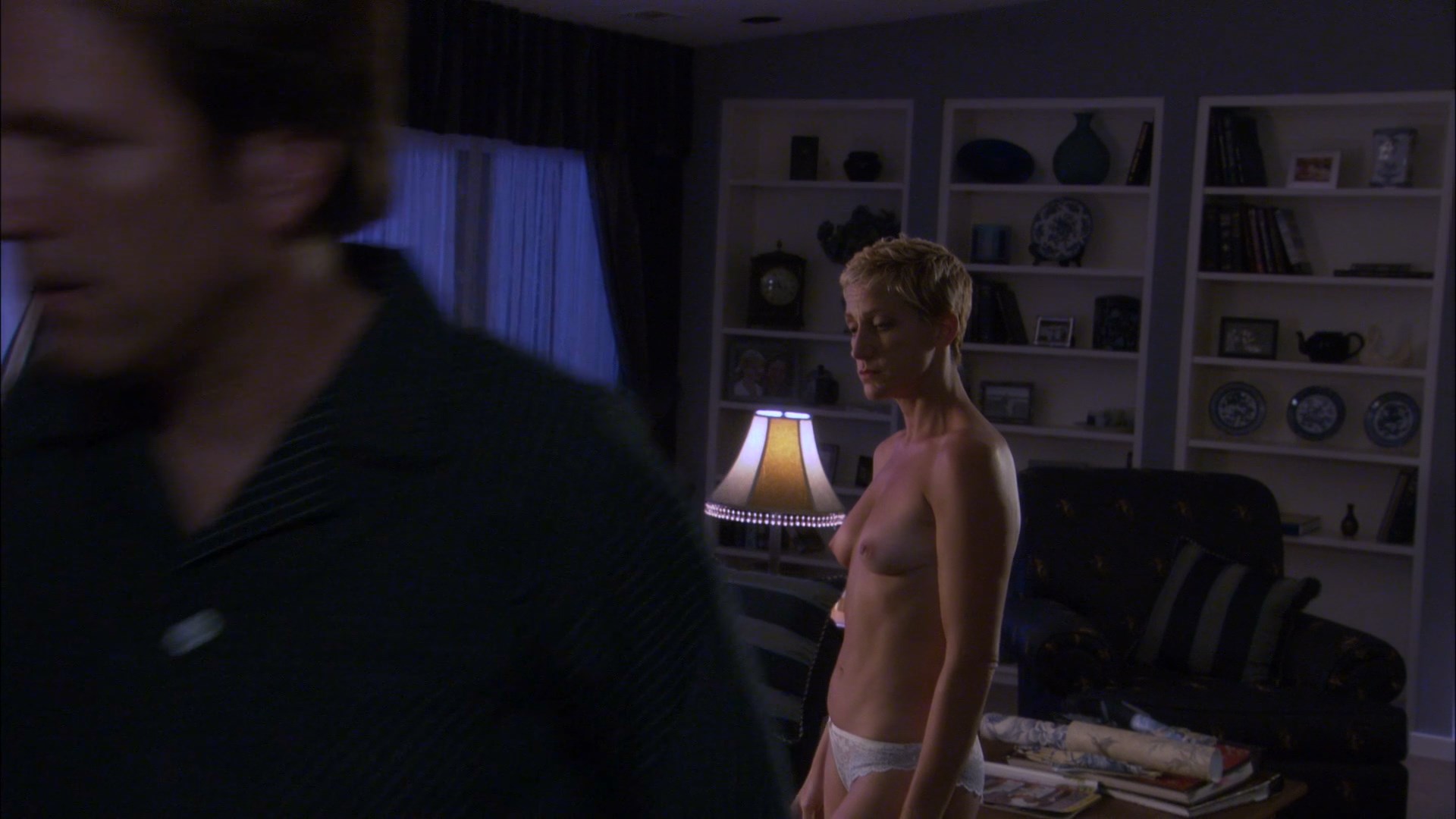 Topless Edie Falco is walking around the room. 